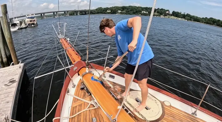 Crew member scrubbing the teak deck of a sailboat tied up at a dock